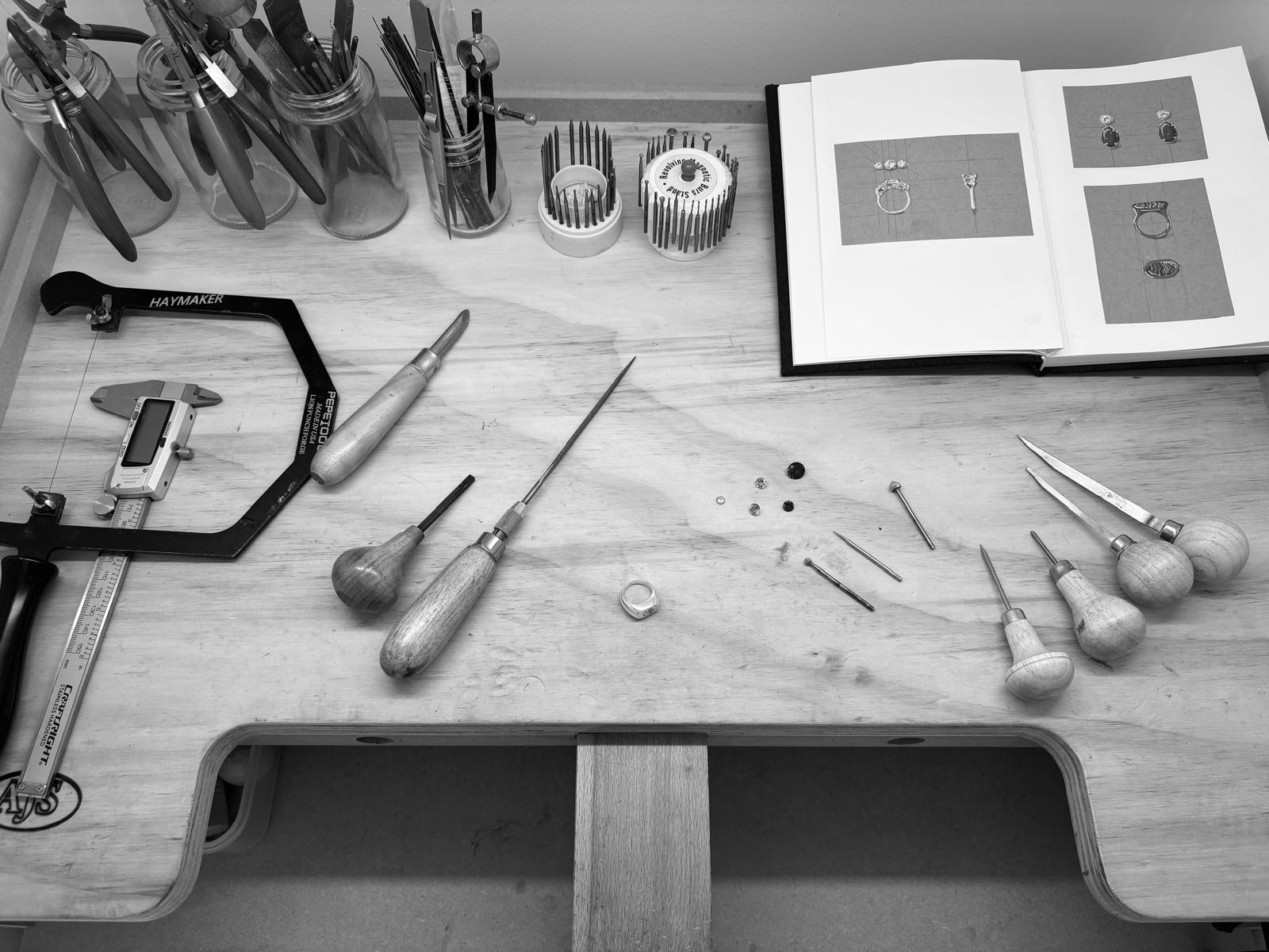 Hayley's jeweller's bench — gravers and hand tools, a sketchbook of ring designs, loose stones and a ring in progress